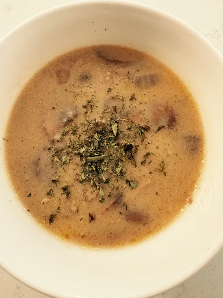 A bowl of mushroom soup topped with parsley flakes.